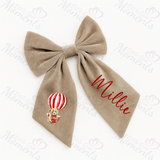 Beige hair bow with 'Millie' and a teddy bear in a hot air balloon design on a white background.