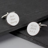 Round silver cufflinks with engraved text on a dark surface