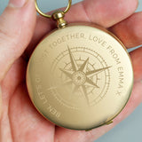 Gold pocket watch with engraved design held in a hand against a neutral background
