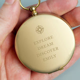 Gold pocket watch with engraved text held in a hand against a neutral background