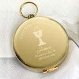 Gold pocket watch engraved with 'First Holy Communion' and personalized details on a white fabric background.