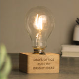 Light bulb on a wooden base with 'Dad's Office Full of Bright Ideas' text, blurred background