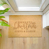 Personalized Christmas doormat with 'Merry Christmas Steve & Robbie' text on a wooden floor.