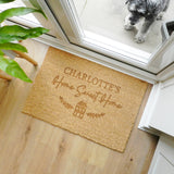 Doormat with 'Charlotte's Home Sweet Home' text on a wooden floor, with a dog looking through a glass door in the background.