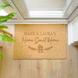 Doormat with 'Mark & Laura's Home Sweet Home' text on a wooden floor.