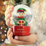 Hand holding a snow globe with an elf figure and personalized text against a festive background.