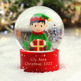 Christmas snow globe with an elf holding a gift, personalized for Lily Anne 2022, against a blurred festive background.