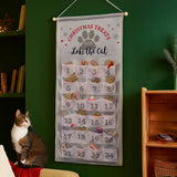 Cat-themed Christmas treats advent calendar hanging on a green wall with a cat sitting below.