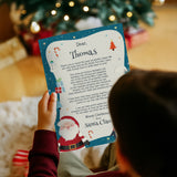 Child holding a letter from Santa Claus in front of a Christmas tree.