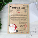 Personalised Santa Letter addressed to Thomas. Laid flat on grey wooden flooring with Christmas tree and fairy lights in the top corner.