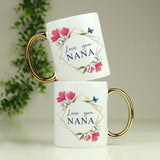 Two white mugs with floral design and 'Love you Nana' text, stacked on a light surface with greenery in the background.