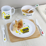 Lifestyle image of 3 piece vehicle cutlery set pictured alongside matching mug, bowl and plate. Plate has on it 2 small triangles of toast and bowl contains spoon and cereal