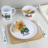 Children's meal set with personalized items including a plate, cup, bowl, and cutlery on a wooden surface.