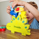 Child playing with a colorful toy dinosaur named 'Freddie' on a wooden surface.