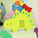 Colorful dinosaur-shaped wooden toddler toy with personalised birth details, placed on a surface with a globe in the background.