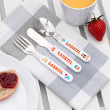 Personalized cutlery set with 'GABRIEL' on a table setting with a cup, plate, and strawberry.