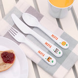 Children's cutlery set with 'MAYA' branding on a table with a plate and mug.
