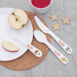 Children's cutlery set with animal designs on a plate with apple slices and a cup of juice.