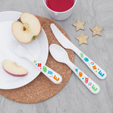A set of plastic cutlery for kids, featuring colourful shapes and the letter 'E' on a wooden table. The set includes a fork, knife, and spoon.
