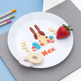 White plate with a cartoon bunny design and the name 'Max'. On the plate is 2 party rings biscuits and a strawberry. On grey placemat.