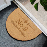 A personalized ornate half moon indoor doormat with text on it, placed on a floor mat, with a window in the background.
