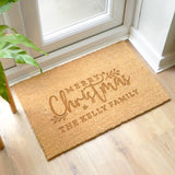 A rectangular beige indoor doormat with 'Merry Christmas' text and a Christmas tree symbolism, placed on a floor mat.
