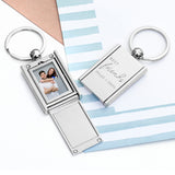 A silver-colored keyring with a photo frame design, engraved with the text 'Best Friends' and a name, placed on a striped background.