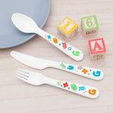 A set of plastic cutlery for kids, featuring colourful shapes and the letter 'G' on a wooden table. The set includes a fork, knife, and spoon.
